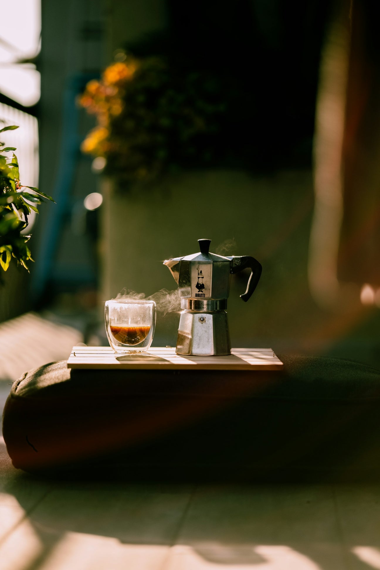 A stovetop moka pot beside a small glass of coffee